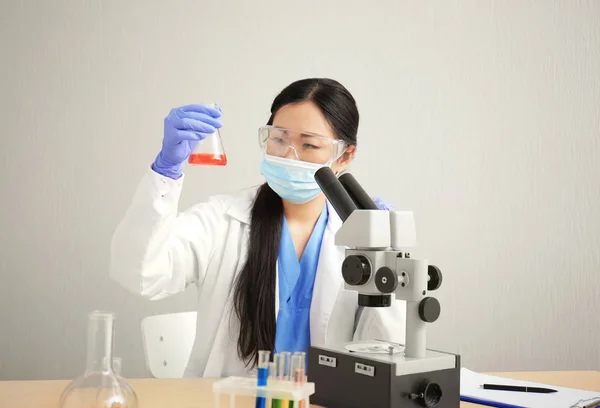 Young doctor working with microscope at table on light background — Stock Photo, Image