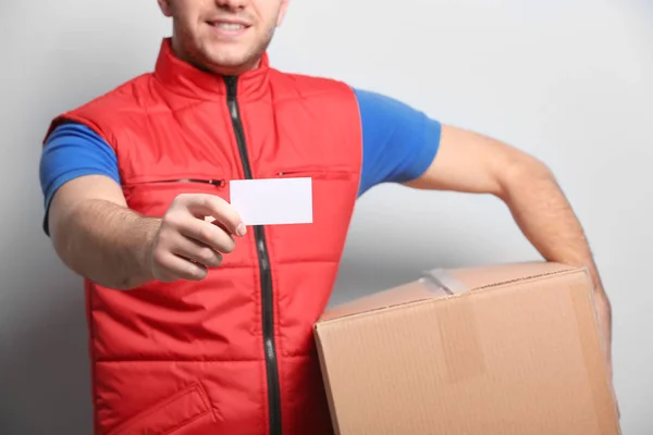 Handsome courier with business card and parcel on light background, closeup — Stock Photo, Image