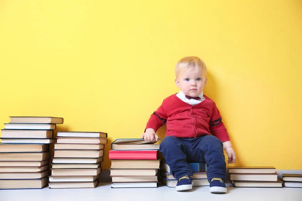 Cute little boy with plenty of books near color wall — Stock Photo, Image