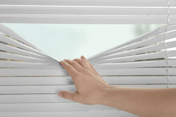 Weibliche Hand trennt Lamellen von Jalousien, um durch Fenster zu sehen — Stockfoto