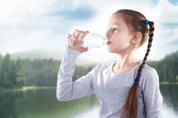 Liten flicka med flaska rent vatten på landskapet bakgrund — Stockfoto