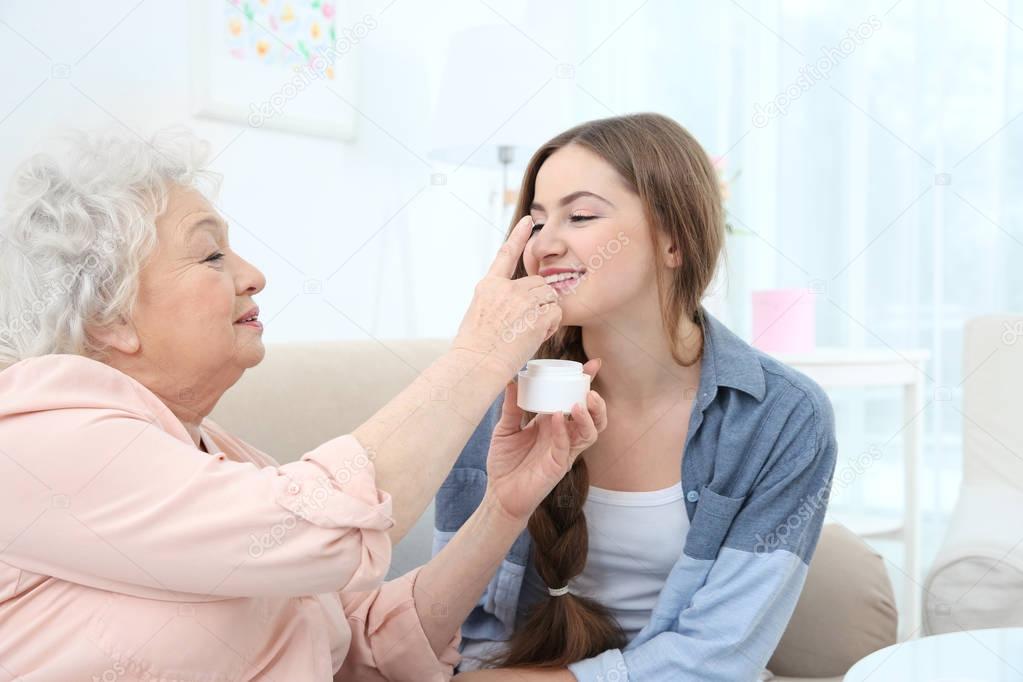 Beautiful girl and grandmother taking skin care on couch at home
