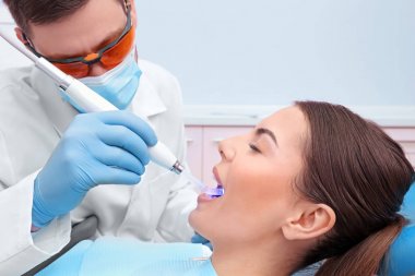 Klinikte dişçi hastanın dişlerini muayene ediyor.
