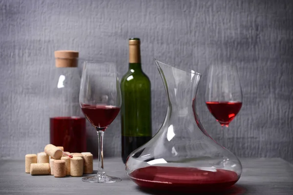 Decantador y vasos con vino tinto sobre mesa sobre fondo gris — Foto de Stock