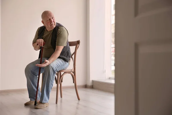 Starší muž s mincemi sedí na židli v prázdné místnosti. Koncept chudoby — Stock fotografie