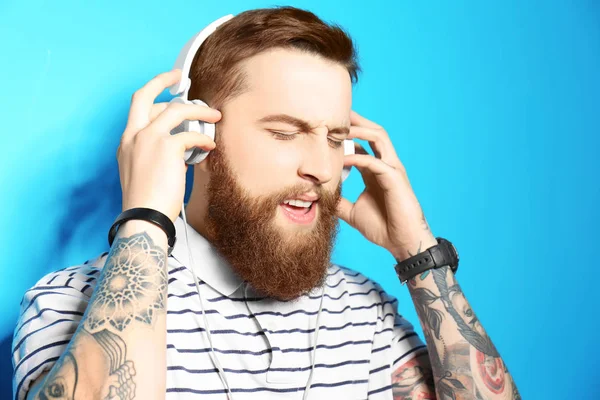 Jeune homme barbu écoutant de la musique avec des écouteurs sur fond bleu — Photo