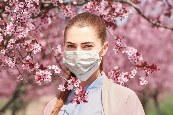 Chica joven con mascarilla entre los árboles en flor en el parque —  Fotos de Stock