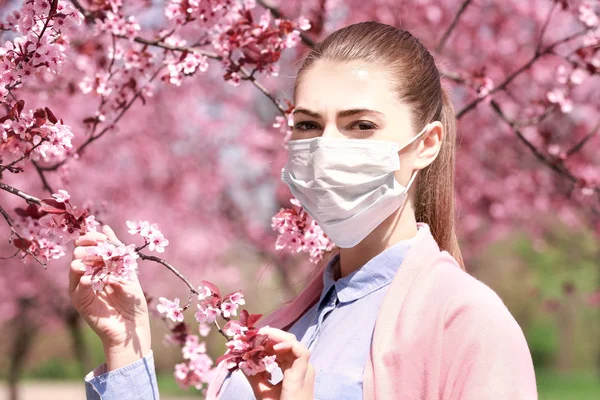 Chica joven con mascarilla entre los árboles en flor en el parque — Foto de Stock