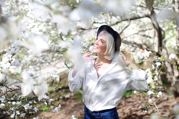 Młoda dziewczyna w kapeluszu w pobliżu kwitnące drzewo magnolia na niewyraźne tło — Zdjęcie stockowe
