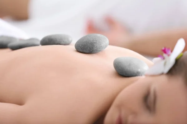 Junge Frau lässt sich im Wellness-Salon mit Steinen massieren — Stockfoto