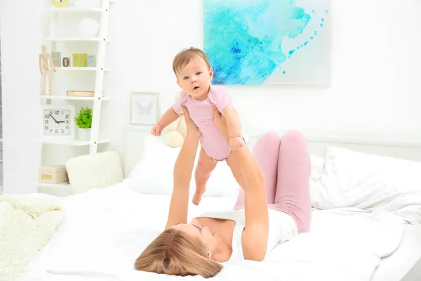 Jovem mãe brincando com seu bebê na cama — Fotografia de Stock