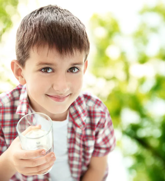 Liten pojke med glas rent vatten på suddig bakgrund — Stockfoto