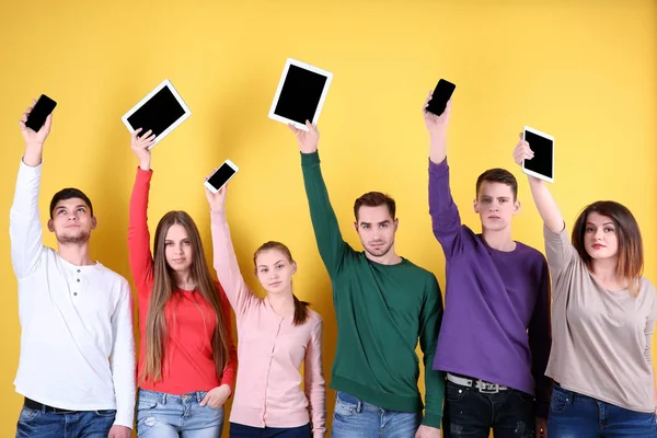 Jovens levantando as mãos com dispositivos digitais no fundo de cor — Fotografia de Stock