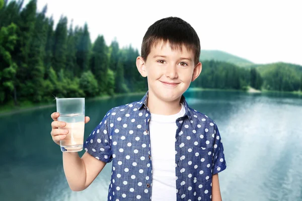 Μικρό αγόρι με ποτήρι καθαρό νερό σε φόντο τοπίο — Φωτογραφία Αρχείου