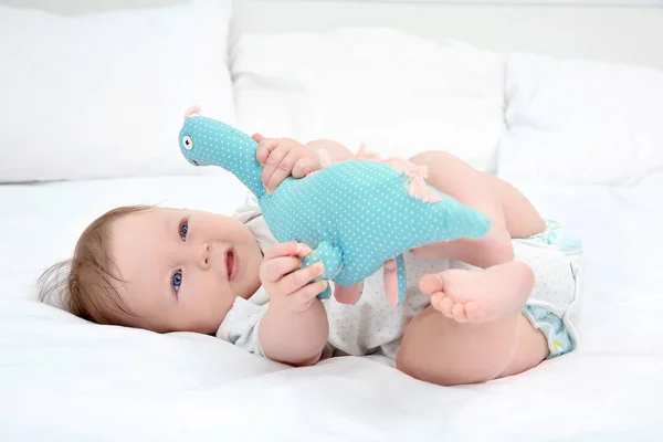 Bebê bonito brincando com dinossauro brinquedo na cama — Fotografia de Stock