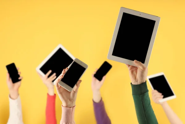 Αυξάνοντας τα χέρια οι νέοι με ψηφιακές συσκευές σε χρώμα φόντου — Φωτογραφία Αρχείου