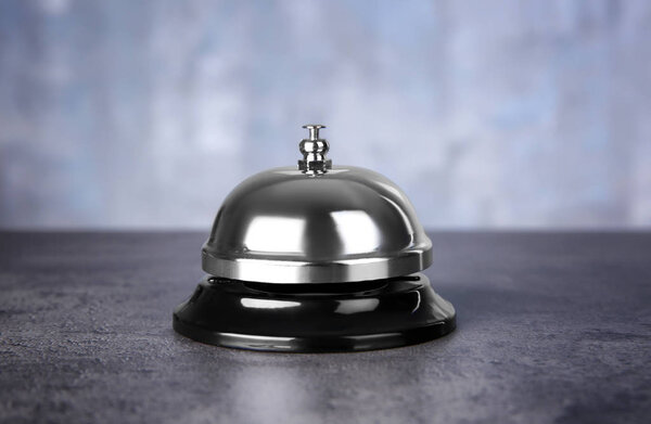 Silver service bell on wooden table against light background