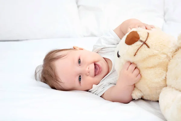 Bebê bonito brincando com ursinho na cama — Fotografia de Stock