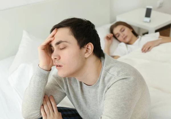 Schläfriger junger Mann sitzt zu Hause auf Bett — Stockfoto