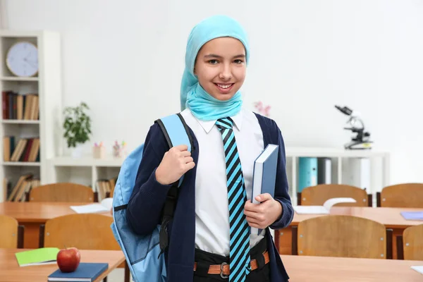 Nettes Mädchen mit Rucksack und Buch steht im Klassenzimmer — Stockfoto