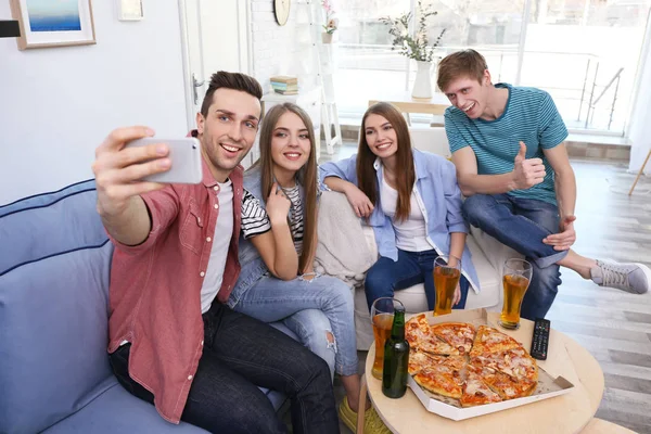 Friends taking selfie while eating pizza at home
