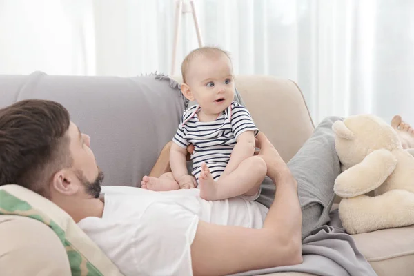 Father lying with cute baby daughter on sofa at home — Stock Photo, Image