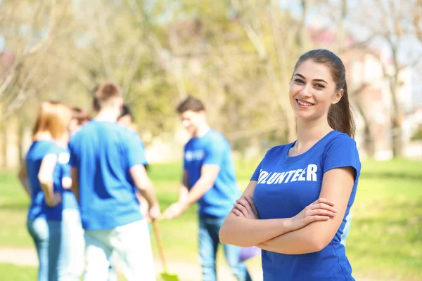 Beautiful young volunteer with team outdoors — Stock Photo, Image