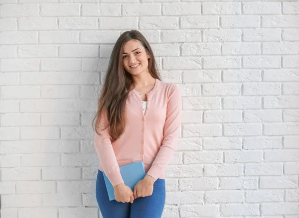 Belle jeune femme avec livre debout près du mur de briques — Photo