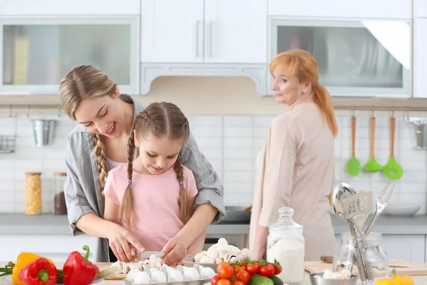 Молодая женщина, ее дочь и мать готовят на кухне — стоковое фото