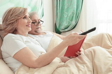 Kitap okuma ve evde yatakta istirahat ederken Tv izlerken yaşlı çift