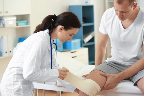 Ортопед накладывает повязку на колено пациента в клинике — стоковое фото