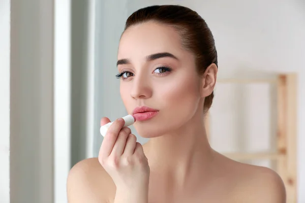 Hermosa joven con lápiz labial sobre fondo borroso — Foto de Stock