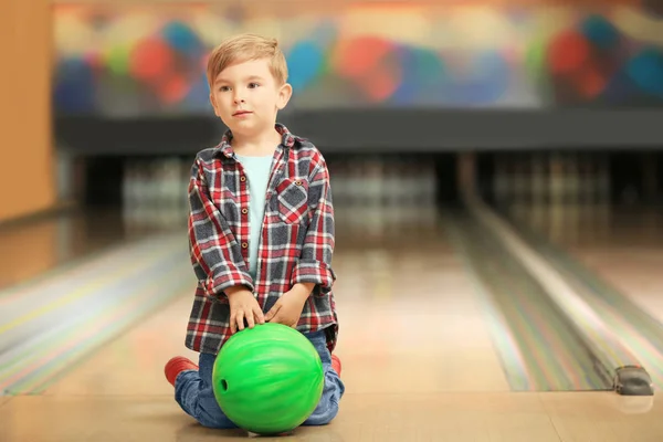 Lindo niño pequeño con bola sentado en el suelo en el club de bolos — Foto de Stock