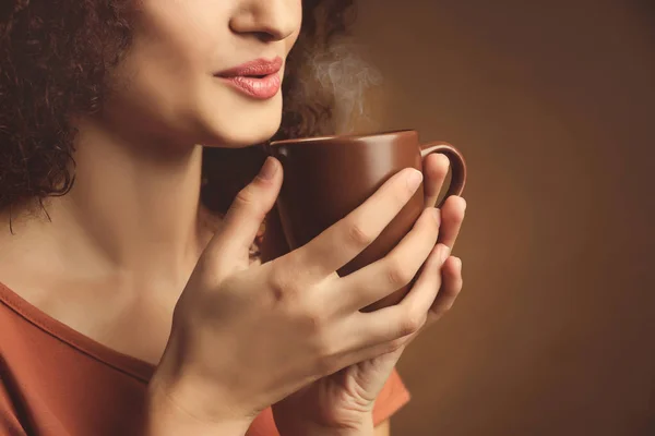 茶色の背景にコーヒーのカップを持つ若い美しい女性の肖像画 — ストック写真