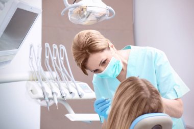 Klinikte dişçi hastanın dişlerini muayene ediyor.