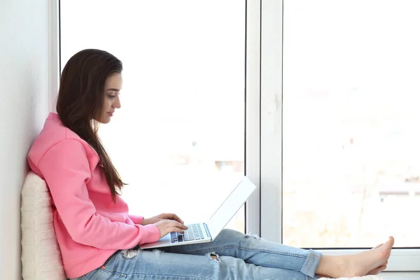 Frau sitzt auf Fensterbank und benutzt Laptop — Stockfoto