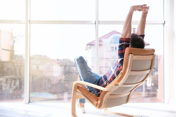 Onnellinen nuori mies istuu nojatuolissa ja venyttelee itseään — kuvapankkivalokuva