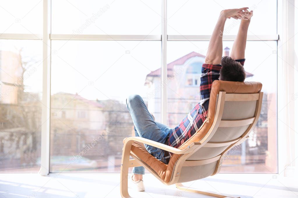 Happy young man sitting in armchair and stretching himself