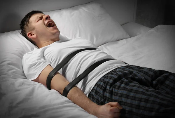 Young man tied up with belts in bed — Stock Photo, Image