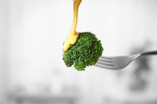 Garpu dengan brokoli dan menuangkan saus keju pada latar belakang yang kabur — Stok Foto