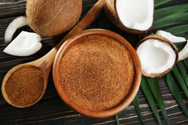 Tigela e colher de açúcar mascavo com coco sobre fundo de madeira — Fotografia de Stock