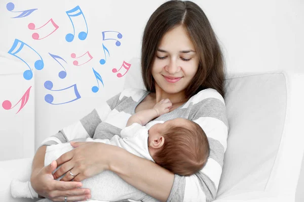 Mãe com bebê dormindo sentado em poltrona. Canções de embalar e conceito de música — Fotografia de Stock