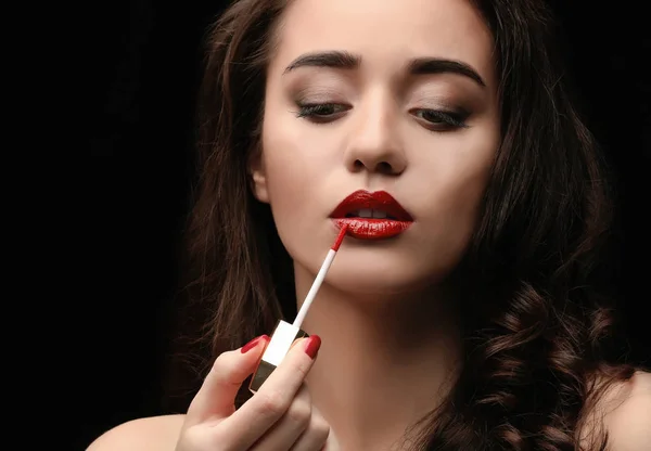 Retrato de mujer hermosa aplicando lápiz labial sobre fondo oscuro — Foto de Stock