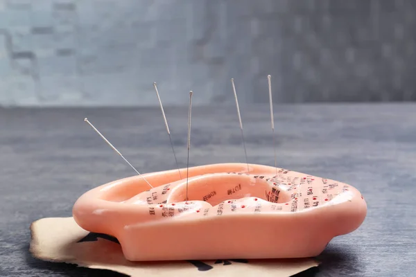 Иголки иглоукалывания в модели уха на сером столе — стоковое фото