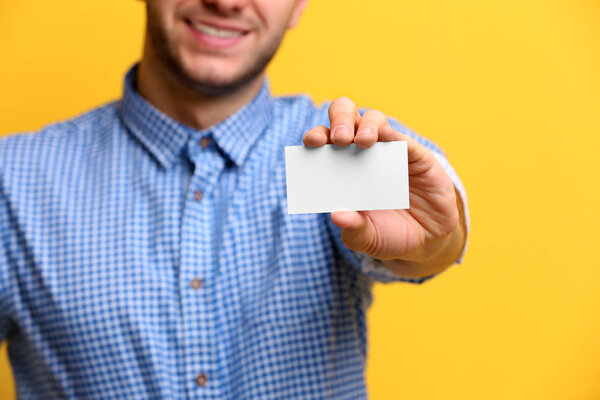 Young man with business card on color background, closeup