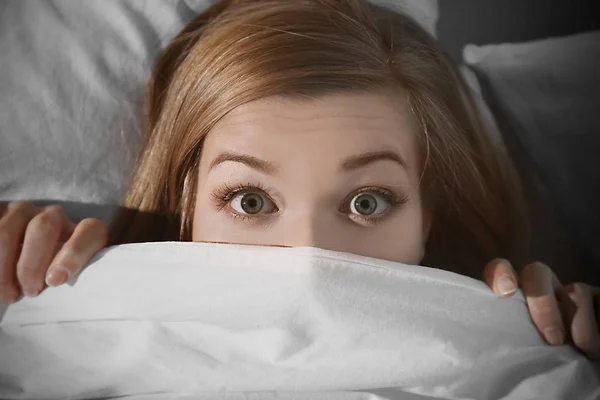 scared woman hiding under blanket