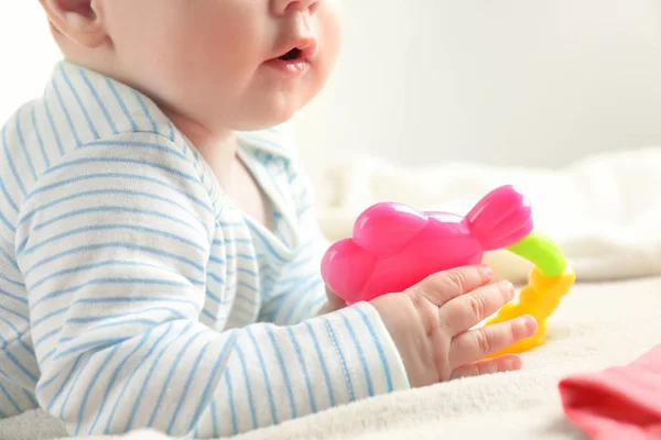 Cute baby holding toy rattle on bed, closeup — Stock Photo, Image