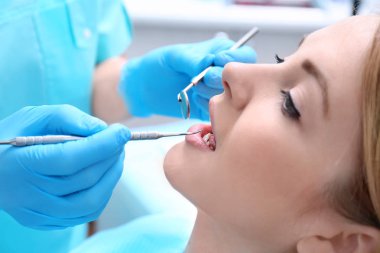 Klinikte dişçi hastanın dişlerini muayene ediyor.