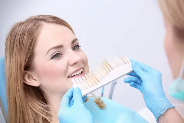 Dentist checking and selecting color of young woman's teeth — Stock Photo, Image