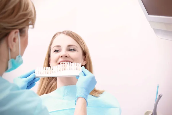 Dentist checking and selecting color of young woman's teeth — Stock Photo, Image